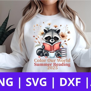 May include: A white sweatshirt with a graphic of a raccoon reading a book and a cup of coffee. The graphic is surrounded by flowers and the text "Color Our World Summer Reading 2025".