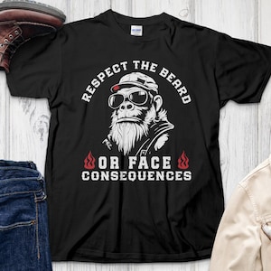 May include: Black t-shirt featuring a gorilla wearing sunglasses and a hat, with the text "Respect the Beard or Face Consequences." The design includes flames. The shirt is displayed with boots, jeans, and a jacket.