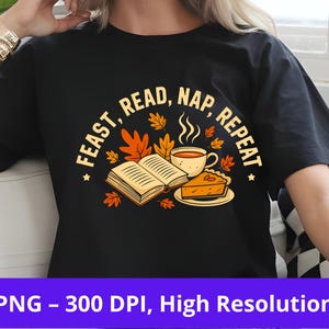以下が含まれることがあります： 秋をテーマにしたグラフィックがプリントされた黒いTシャツ。「FEAST, READ, NAP, REPEAT」の文字が本、ティーカップ、パイの周りに配置され、紅葉で囲まれています。高解像度PNG画像です。