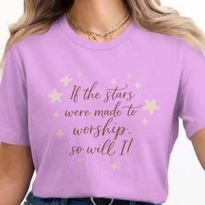 Peut inclure: T-shirt lilas avec l'inscription "If the stars were made to worship, so will I!" en écriture cursive. Le motif comprend des étoiles beiges.