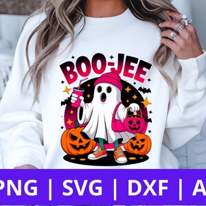 May include: White sweatshirt with a Halloween-themed graphic. The design features a cartoon ghost wearing a pink beanie, holding a drink and a pumpkin-shaped bag, with the text "BOO-JEE". Two orange pumpkins are on either side.