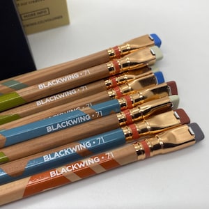 Puede incluir: Primer plano de varios lápices Blackwing 71. Los lápices tienen un cuerpo de madera con un diseño de rayas diagonales en varios colores, incluyendo verde, azul y naranja. Cada lápiz tiene una virola dorada y una goma de borrar de color.