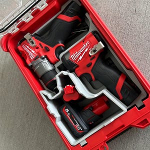 以下が含まれることがあります： 透明な蓋が付いた、赤と黒のミルウォーキー電動工具キット。キットには、ドリル、インパクトドライバー、バッテリーが含まれており、すべてカスタムグレーのフォームインサートに収められています。