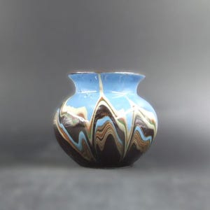 May include: A small, round ceramic vase with a light blue rim and interior. The exterior features a swirling pattern of brown, white, and blue colours. The vase has a wide body and a slightly flared opening, suitable for displaying flowers.
