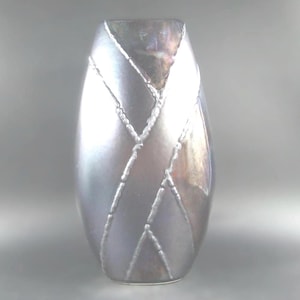 May include: An oval-shaped vase with a pearlescent, silver finish. The vase has a network of raised, silver lines forming a geometric pattern. The top of the vase has a darker, iridescent sheen, adding depth to the design.