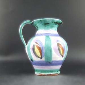 May include: A ceramic pitcher with a green handle and rim, hand-painted with a colourful design. The body has vertical green and white stripes, with horizontal purple and blue stripes. Decorative oval shapes with yellow and brown accents are painted on the front.