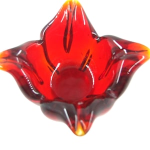 May include: A striking red glass bowl, shaped like a flower. The bowl features a central, rounded area and petal-like edges, with a colour gradient from red to amber and yellow. The glass is transparent.