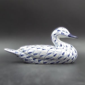 May include: A ceramic duck figurine with a white base and blue feather-like patterns. The duck has a curved neck and a dark blue beak. The figurine is a decorative item.