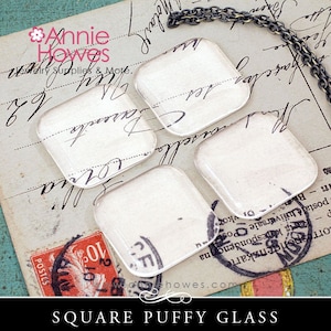 May include: Four square, puffy glass pieces with a vintage paper design, on a background of aged paper with script. A silver chain is visible at the top. The text "SQUARE PUFFY GLASS" is at the bottom.