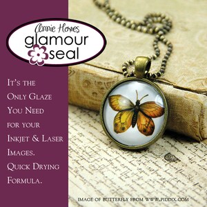 May include: A gold-toned necklace with a round pendant featuring a butterfly image. The pendant is on a book with old writing. The text on the image reads "Annie Howes glamour seal It's the only glaze you need for your inkjet & laser images. Quick drying formula."
