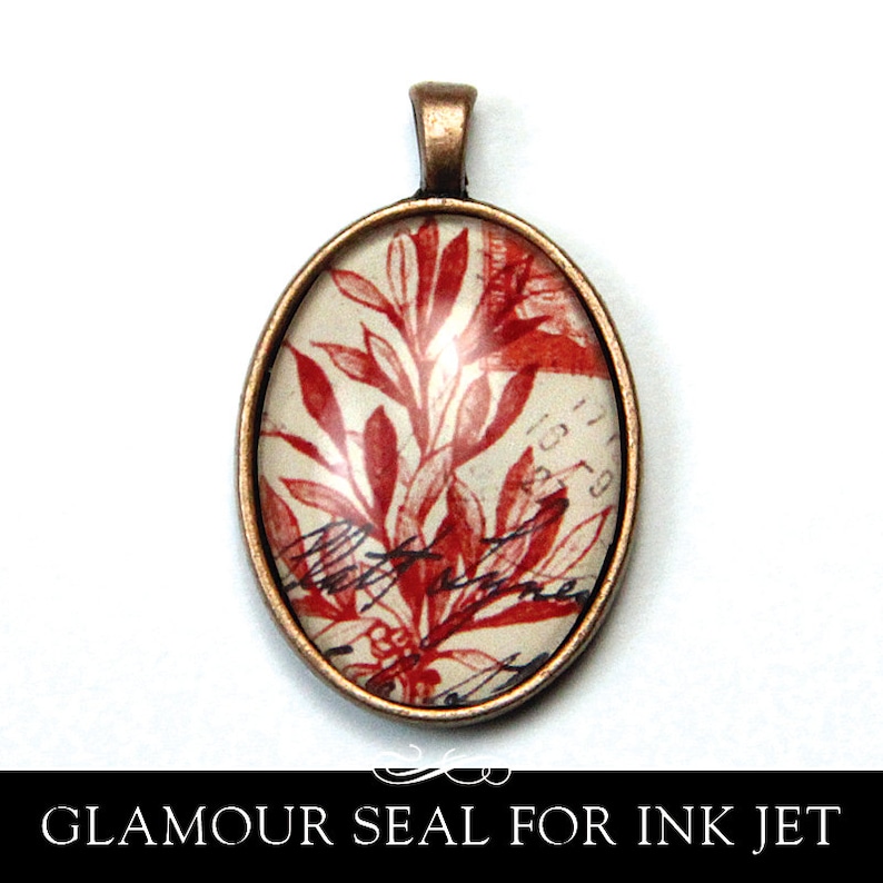 May include: A copper oval pendant with a glass insert featuring a red floral design on a white background. The pendant has a loop at the top for hanging.