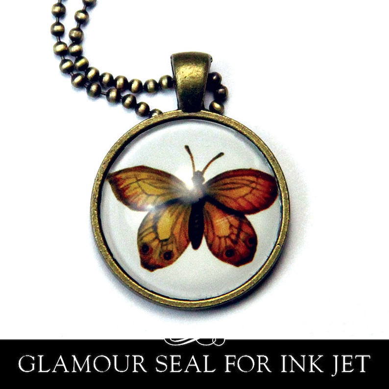 May include: A gold-toned pendant necklace with a round glass charm featuring a detailed illustration of a butterfly with orange and brown wings. The butterfly is set against a white background.