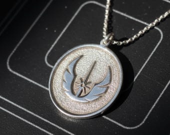 May include: Silver-toned pendant necklace featuring a circular pendant with a textured background and a stylized emblem in blue and silver. The necklace has a delicate chain and is displayed on a dark surface.