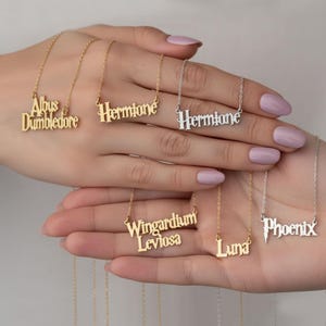 May include: A collection of gold and silver nameplate necklaces. The names include "Albus Dumbledore", "Hermione", "Wingardium Leviosa", "Luna", and "Phoenix". Each necklace has a delicate chain.