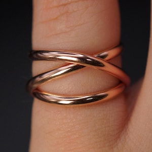 May include: A rose gold ring with a triple band design. The bands are intertwined and create a criss-cross pattern.