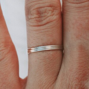 Puede incluir: Primer plano de una mano con un conjunto de tres anillos finos de oro en el dedo anular.