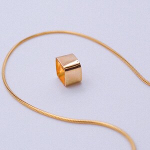 May include: A gold chain necklace with a square pendant. The chain is a snake chain style.