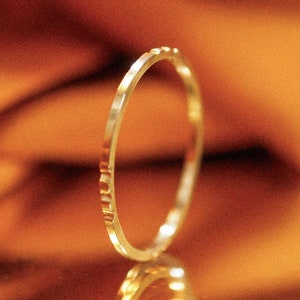 Puede incluir: Un anillo de oro con una superficie texturizada, reflejado en una superficie dorada.