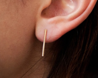 May include: A close-up of a person's ear with a thin gold bar earring.