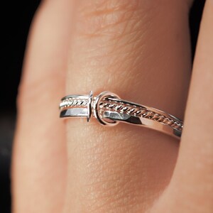 May include: A silver ring with a braided design and a knot detail.