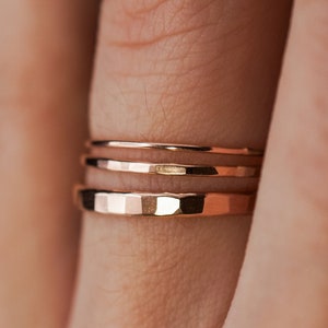 May include: Three gold-toned stacking rings on a finger. The rings are thin and have a hammered texture.