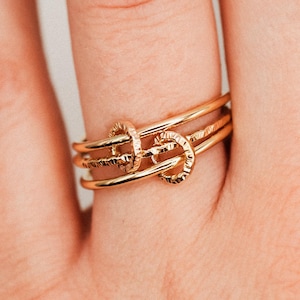 May include: A set of gold rings on a finger. The rings have textured and circular designs. The rings are stacked together, creating a layered effect. The rings are made of a shiny, gold-colored metal.