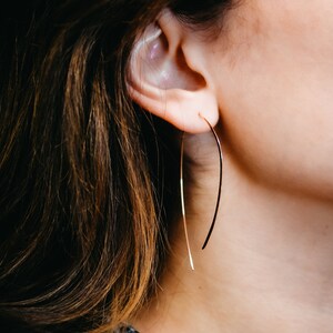 Puede incluir: Una mujer con un pendiente de aro dorado. El pendiente es fino y tiene una forma curva.