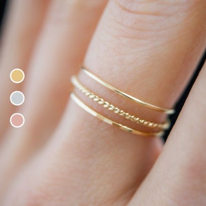 Close up view of three gold stacking rings modeled on a middle finger. One twist ring with one smooth and one hammered ring.