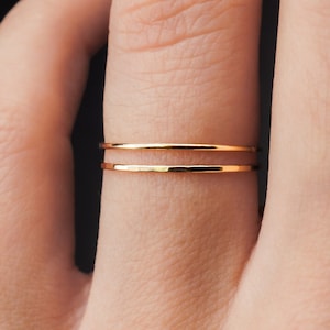 Puede incluir: Dos anillos finos de oro apilados en un dedo. Los anillos son simples y delicados, con una textura martillada.