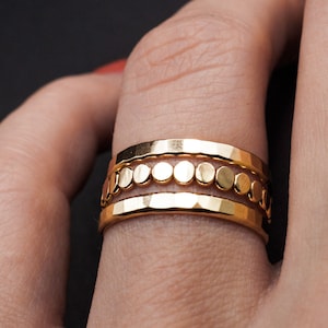 Puede incluir: Un anillo de oro con tres bandas. La banda del medio tiene una fila de pequeñas cuentas redondas de oro.