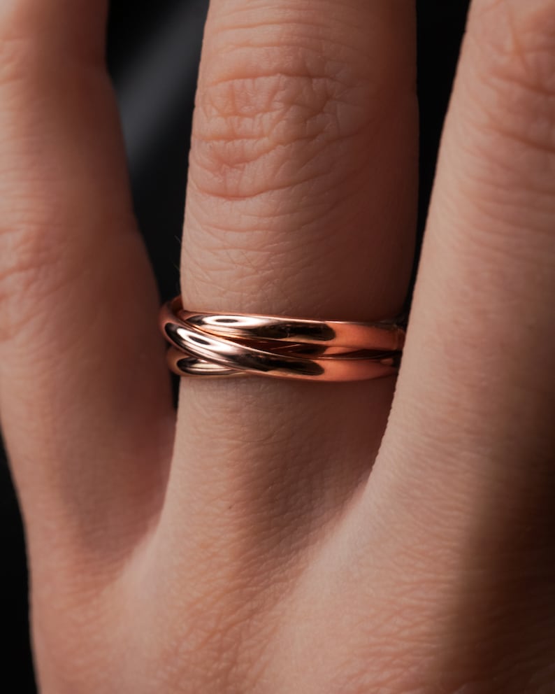 Pu&ograve; includere: Un anello in oro rosa con tre bande intrecciate. L'anello &egrave; indossato su un dito.