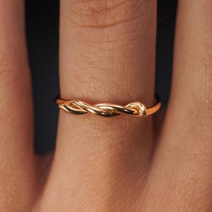 May include: A gold-toned ring with a twisted design. The ring is worn on a finger.