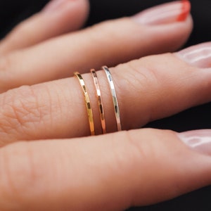K&ouml;nnte beinhalten: Nahaufnahme von vier d&uuml;nnen, geh&auml;mmerten Metallringen in Gold, Ros&eacute;gold und Silber. Die Ringe sind auf einem Finger vor dunklem Hintergrund gestapelt. Die Ringe sind zart und minimalistisch.