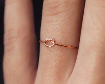 Op de afbeelding: Een delicate roségouden knoop ring aan een vinger.