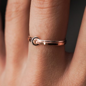 May include: A rose gold ring with a simple, minimalist design. The ring is made of two bands that are intertwined, creating a knot-like shape.