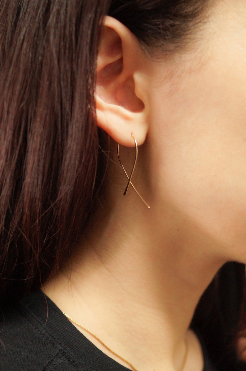 Mini Ribbon Hoops that thread through an earlobe piercing and dangle. Modelled in 14K Gold Fill. Thin wire earrings, easy and functional to wear. Shaped like cancer awareness ribbon.