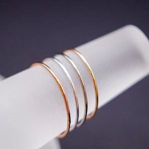 Puede incluir: Cuatro anillos finos de oro, plata y oro rosa apilados en un expositor blanco.