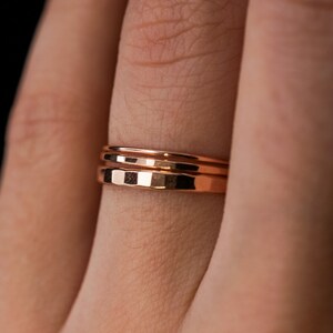 May include: A close-up of a person's finger wearing three thin gold bands.