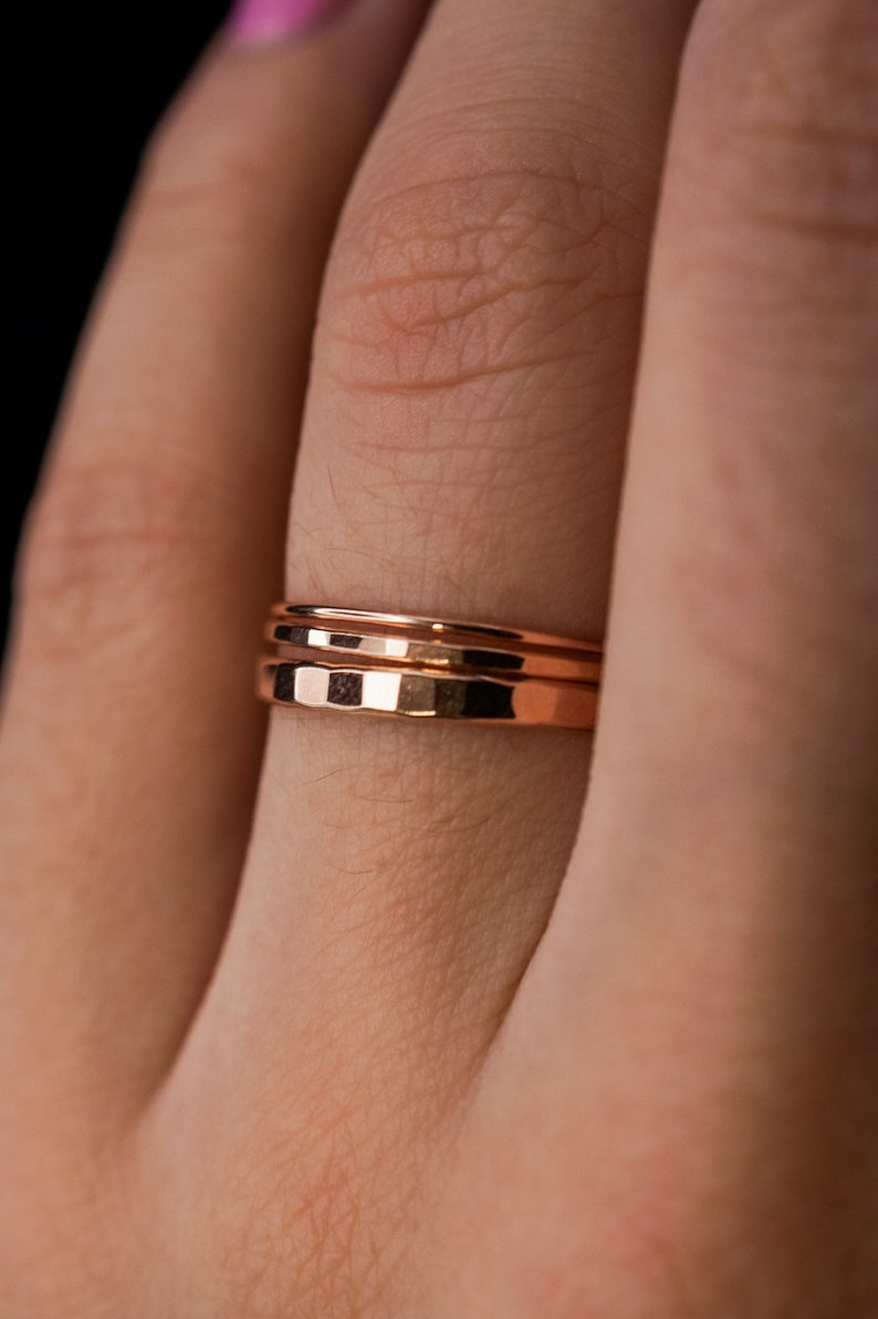 May include: A close-up of a person's finger wearing three thin gold bands.