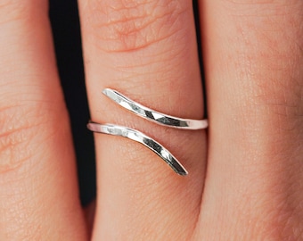 May include: A silver hammered ring with a curved design. The ring is worn on a finger.
