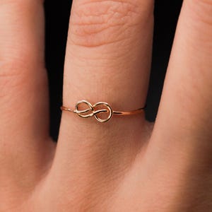 May include: A gold infinity knot ring on a finger.