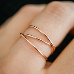 May include: A close-up of a gold ring with three thin bands that are intertwined. The ring is worn on a person's finger.