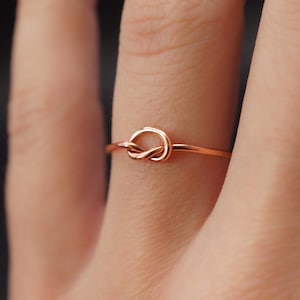 Puede incluir: Un anillo simple de nudo de oro rosa. El anillo es delgado y delicado, con un pequeño nudo en el centro.