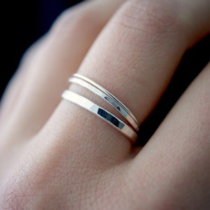 May include: Two silver rings stacked on a finger. The top ring is thin and smooth, while the bottom ring is wider and has a hammered texture.