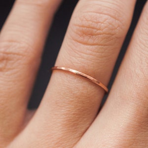 K&ouml;nnte beinhalten: Nahaufnahme eines zarten, d&uuml;nnen ros&eacute;goldenen Rings an einem Finger. Der Ring hat ein schlichtes, minimalistisches Design mit leicht strukturierter Oberfl&auml;che. Der Ring ist im Bandstil gehalten, perfekt zum Stapeln oder einzeln Tragen. Die Farbe des Rings ist ein warmer, metallischer Farbton.