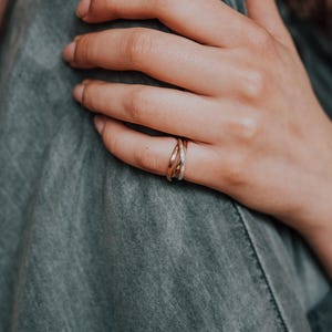 Pode incluir: Um close-up de uma m&atilde;o usando um anel entrela&ccedil;ado de ouro, prata e ouro rosa. O anel est&aacute; no dedo m&eacute;dio da m&atilde;o.