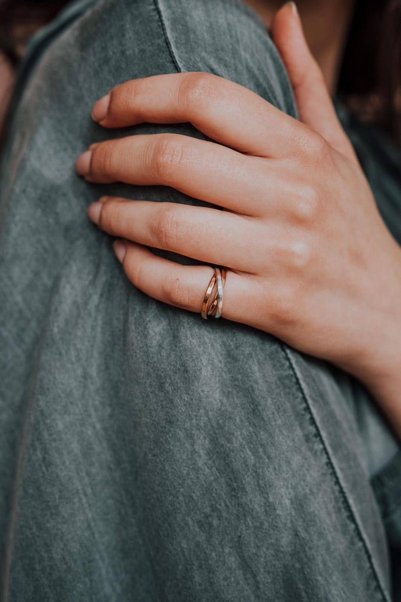 Pode incluir: Um close-up de uma m&atilde;o usando um anel entrela&ccedil;ado de ouro, prata e ouro rosa. O anel est&aacute; no dedo m&eacute;dio da m&atilde;o.