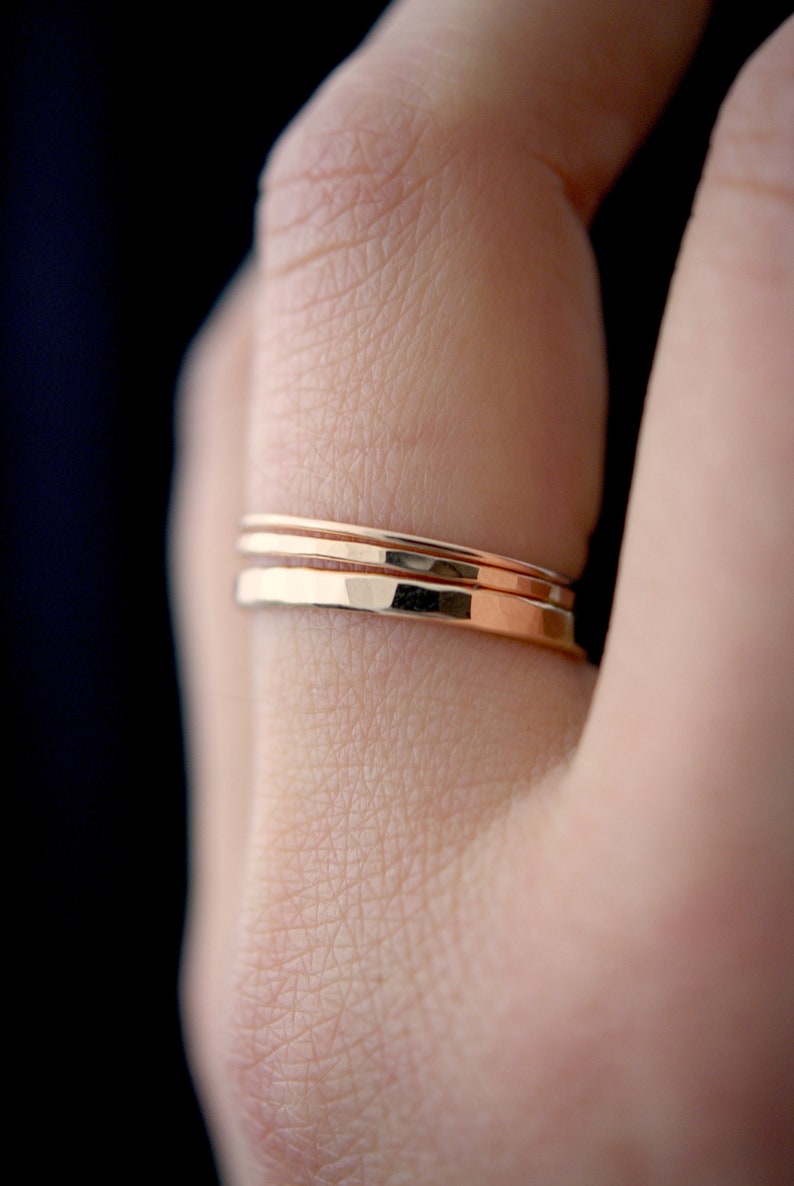 May include: Three thin gold rings stacked on a finger. The rings are smooth and have a slightly hammered texture.