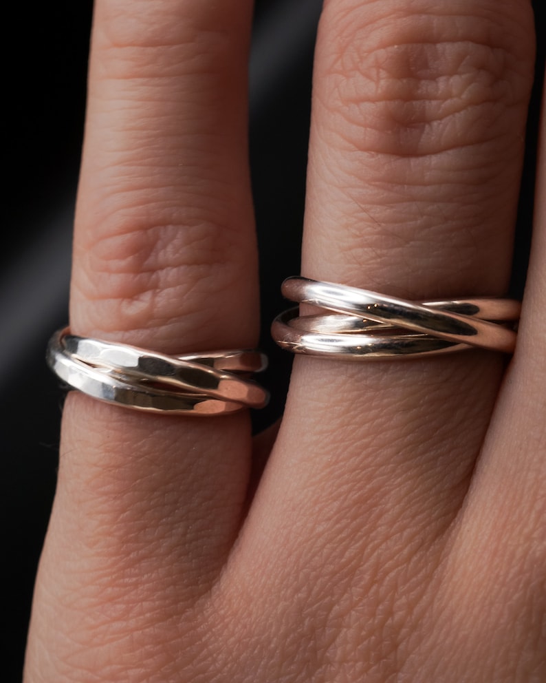 Pu&ograve; includere: Due anelli d'argento indossati su un dito. L'anello a sinistra &egrave; un anello a tripla fascia con una texture martellata. L'anello a destra &egrave; un anello a tripla fascia con una finitura liscia.