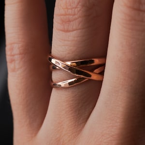 Pu&ograve; includere: Un anello in oro rosa con un design a croce. L'anello &egrave; composto da tre bande intrecciate.